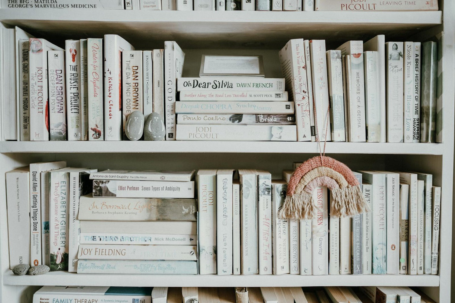 A minimalist bookshelf displaying various books with a tassel decoration, perfect for literary spaces.